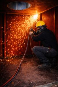 Öltankentsorgung – Zerlegung eines Stahltanks im Tankraum Arbeiter zerlegt einen Stahltank bei der fachgerechten Öltankentsorgung mit Brennschneider